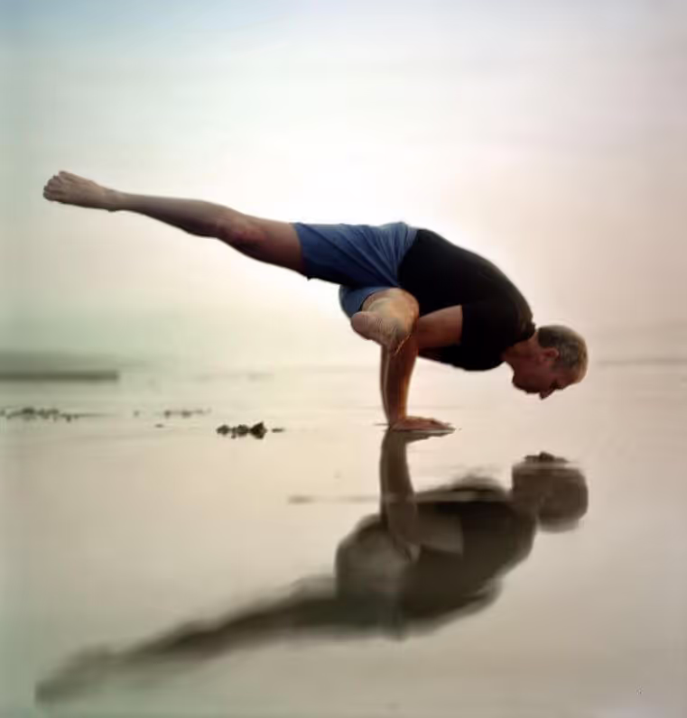 Larry Schultz in an arm balance on a beach at sunrise